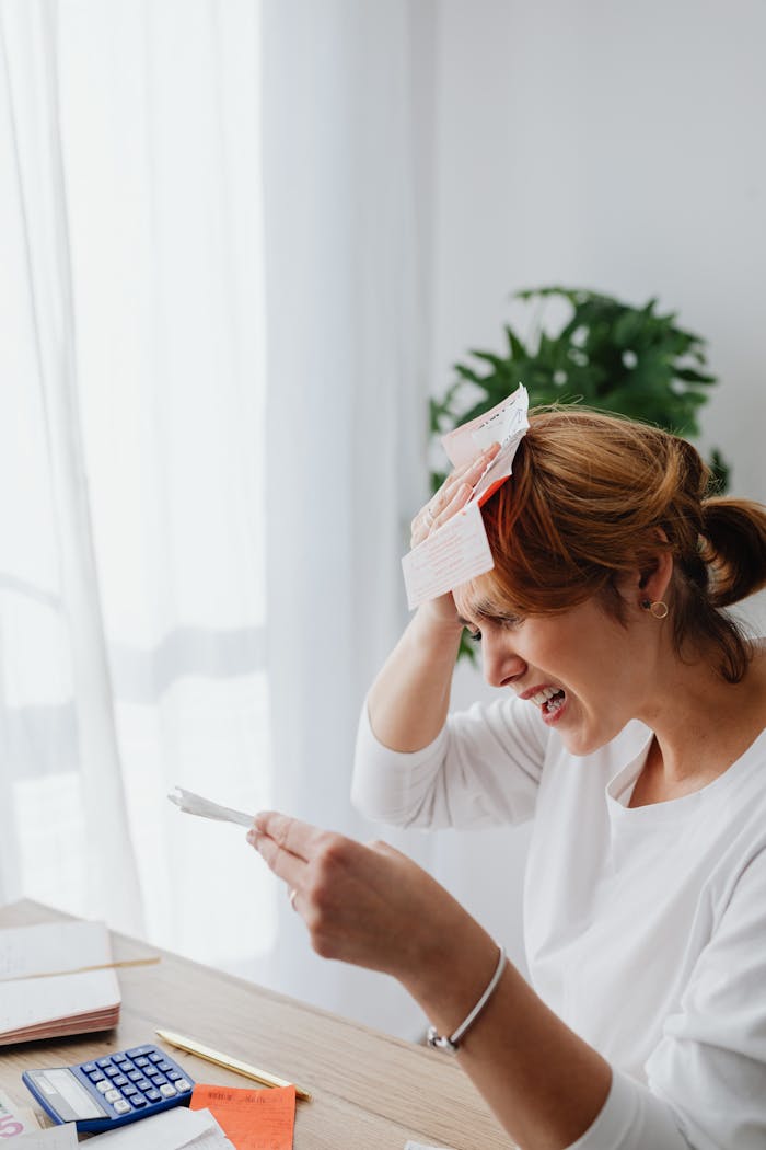 Woman sitting at table stressed about bills in bright living room.